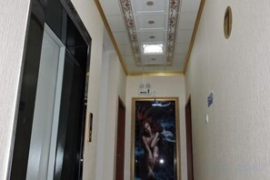 A narrow hallway with a ceiling light fixture, a door with a painting, and a wall-mounted light switch. - Taijinyun Business Hotel (Hechi)