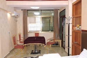 A hotel room with a dining table, chairs, a bed, a coat rack, and a wardrobe.