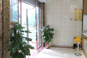 An indoor area with a glass door entrance, potted plants, a yellow chair, and a wall-mounted sign.