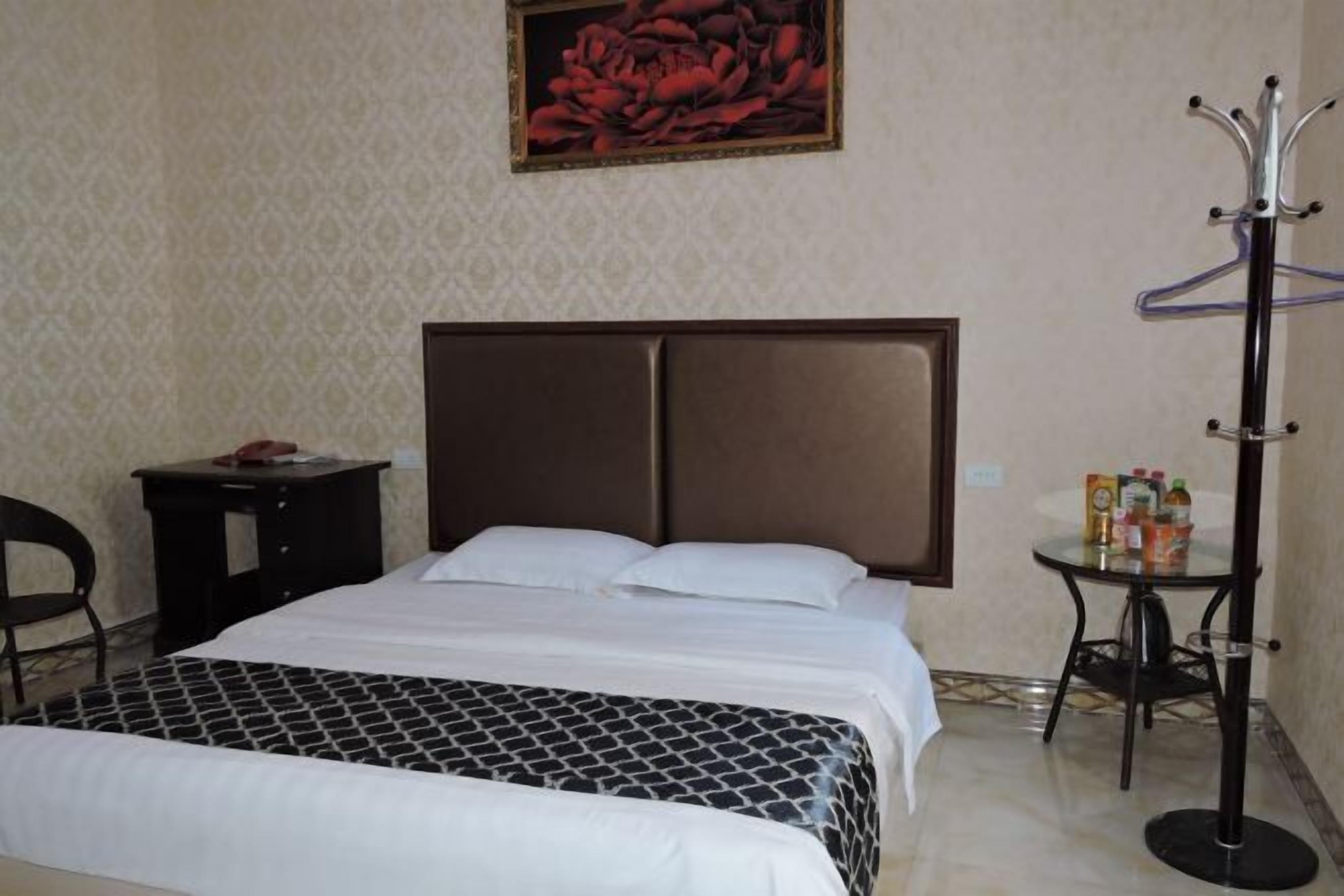 Una habitación de hotel con una cama grande, una mesita con una botella de agua, un perchero y un cuadro en la pared.