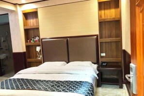 A hotel room with a bed, a bedside table, a small shelf with toiletries, and a wooden headboard.