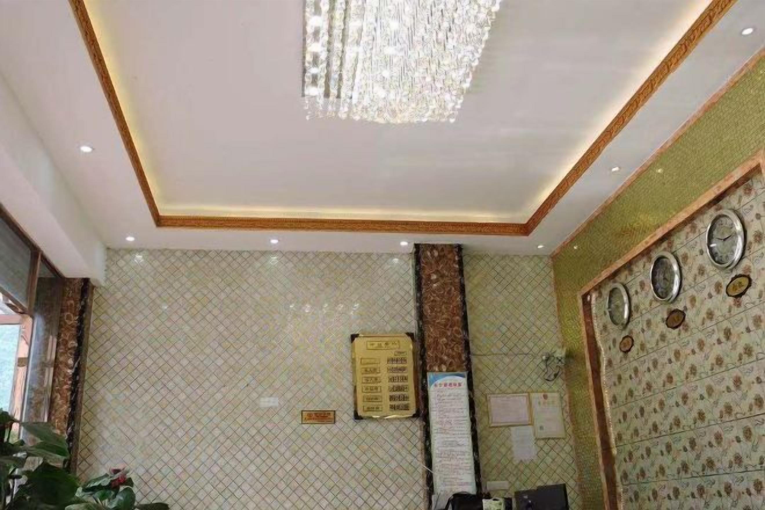 A hotel lobby with a chandelier, patterned walls, a reception desk, and a wall clock.