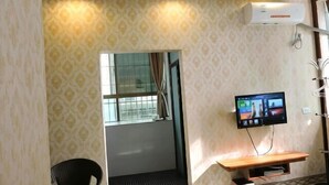 Ett hotellrum med en mönstrad tapet, en tv som är monterad på väggen, en träbänk och ett fönster med gardiner.