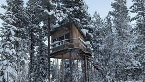 A wooden cabin with a balcony, surrounded by snow-covered trees. - Aurora Lodge (Arvidsjaur)