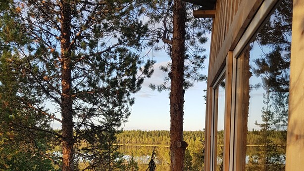 A wooden deck with a railing overlooking a forested area and a lake. - Aurora Lodge (Arvidsjaur)