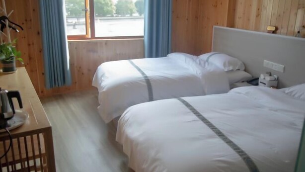A hotel room with two beds, a wooden desk, a window with curtains, and a view of the outside. - Hetianxia Hotel (Wuyuan)