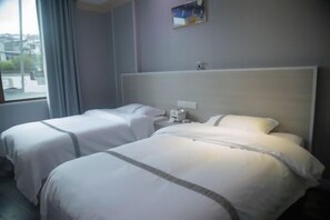 A hotel room with two beds, a window with curtains, a painting on the wall, and a nightstand with a lamp. - Hetianxia Hotel (Wuyuan)