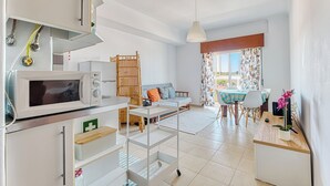 A modern kitchen with a microwave, a wooden rack, and a dining area with a table and chairs. - Over the Rainbow  (Almada)