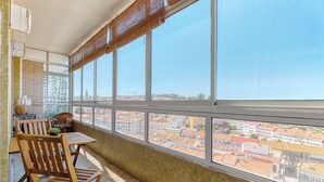 A balcony with a table and chairs, large windows with a city view, and a patterned wall. - Over the Rainbow  (Almada)