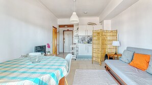 A compact living space with a bed, a dining table, a sofa, a kitchen area, and a bamboo partition. - Over the Rainbow  (Almada)
