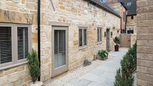 A stone building with multiple windows and doors, a gravel pathway, and potted plants. - A spectacular barn conversion - Highgate (Moreton-in-Marsh)