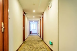 Corredor de hotel com portas de madeira, carpete estampado e tomada elétrica verde.