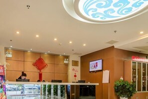 A hotel reception area with a reception desk, a digital screen, and a decorative red emblem on the wall. - Huacheng Express Hotel (Jiangyin)