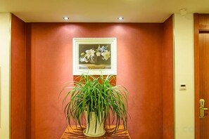 Um corredor com uma planta em vaso, um quadro na parede e uma porta com puxador.