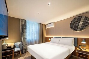 A modern hotel room with a large bed, a desk, and a TV.