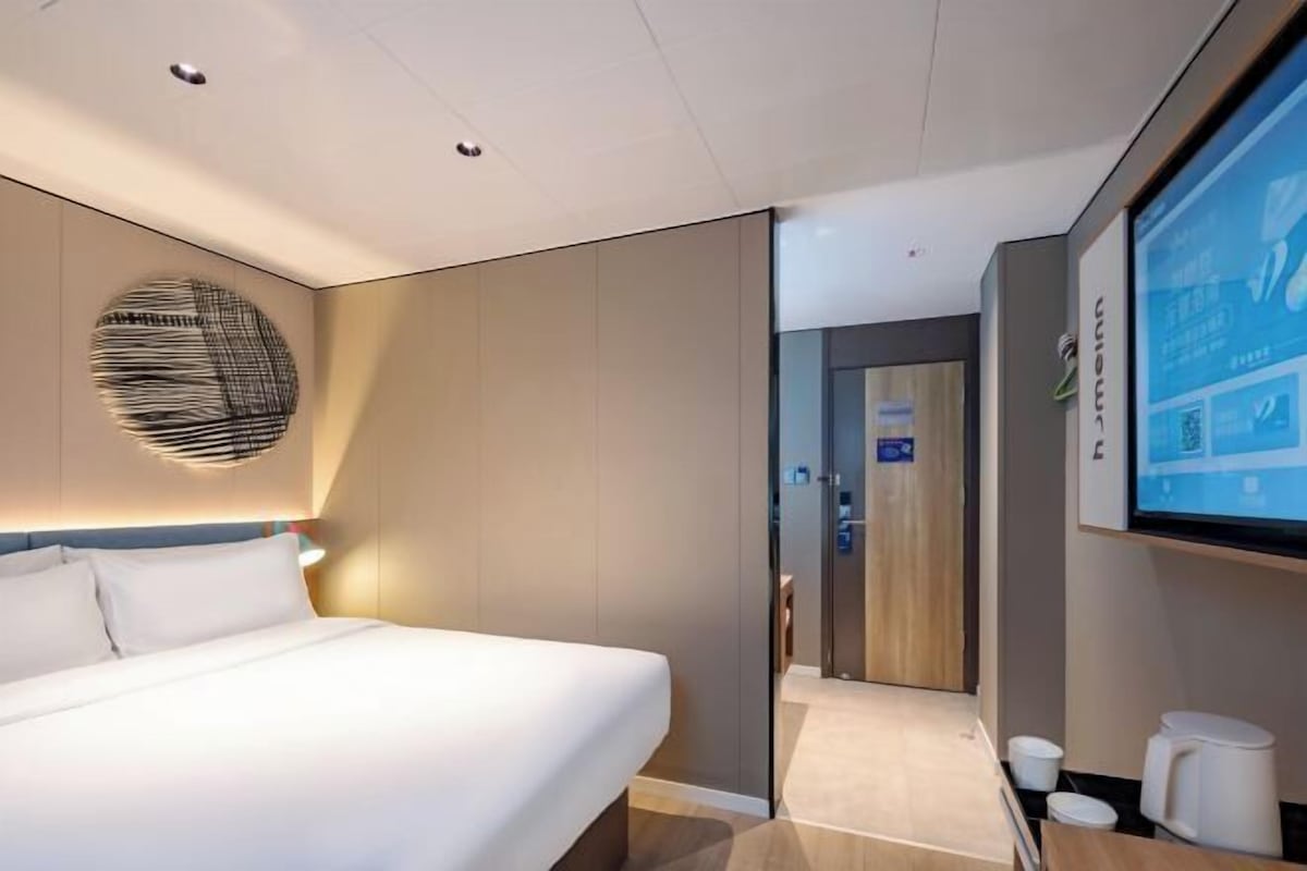 A modern hotel room with a large bed, a wall-mounted TV, and a minimalist decor.