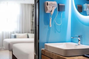 A hotel room with a bed, a bathroom with a sink, and a hairdryer on the wall.