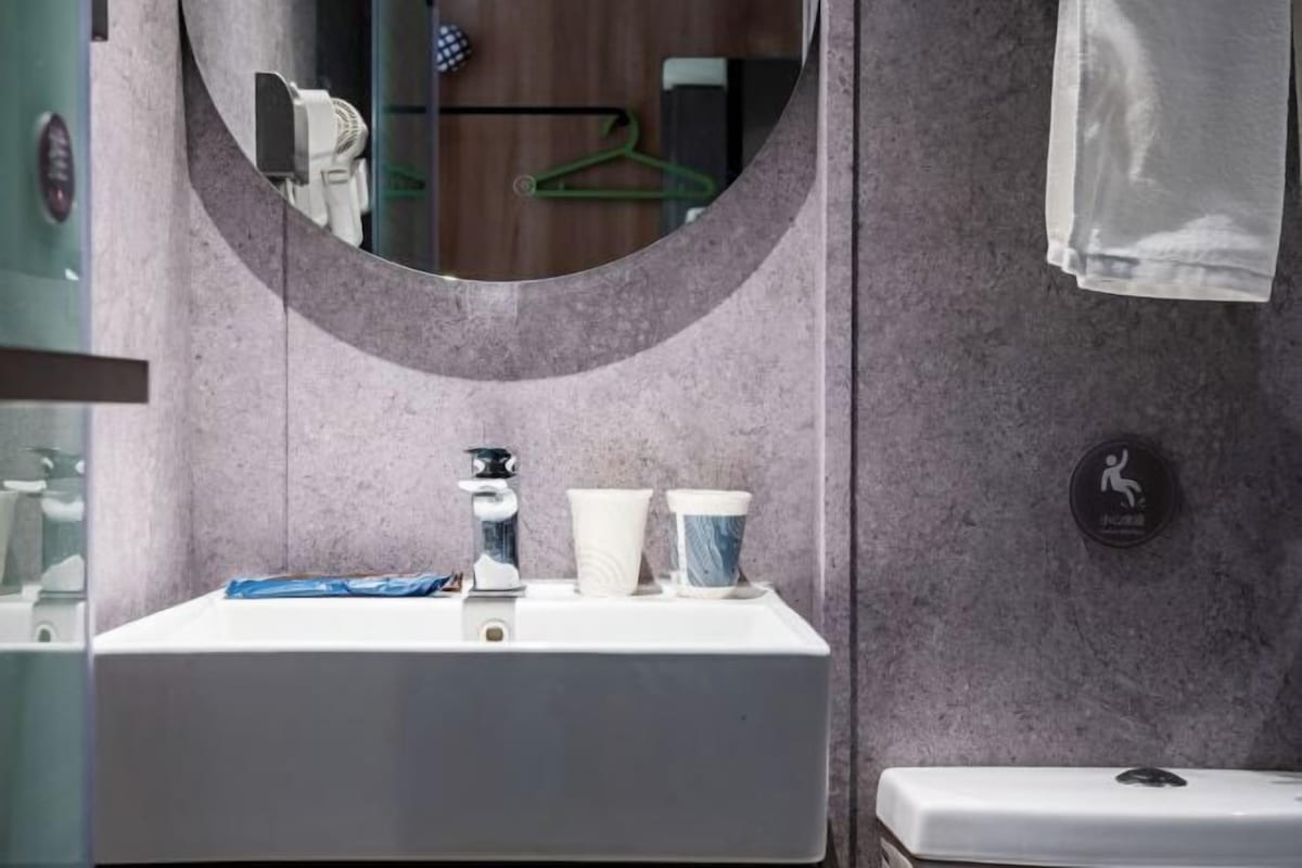 A bathroom with a sink, mirror, towel rack, and a sign indicating a shower area.