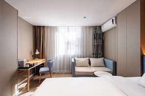 A hotel room with a bed, a desk with a chair, a sofa, and a window with curtains.