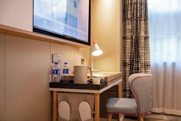 A hotel room with a desk, two chairs, a television, a lamp, and a window with curtains.
