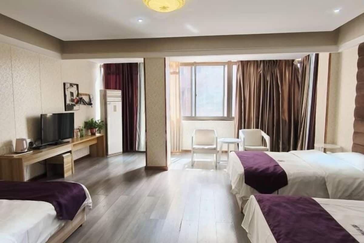 Habitación de hotel con dos camas, un escritorio con televisor, una silla y una ventana con cortinas.
