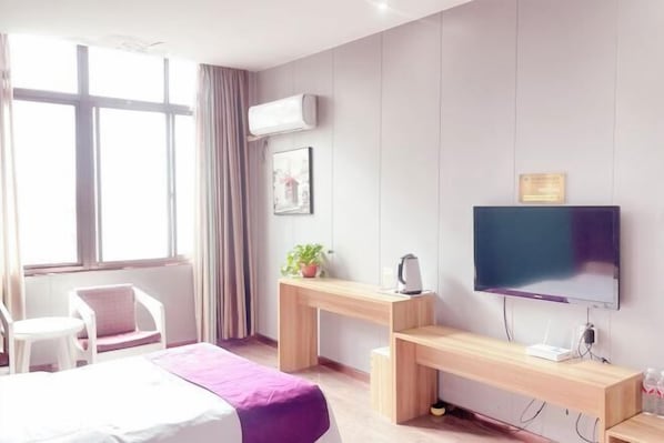 A modern hotel room with a bed, a desk with a computer, a TV, and a window with curtains.