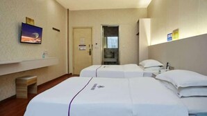 Une chambre d’hôtel avec deux lits, un téléviseur fixé au mur, une petite table et une porte donnant sur une salle de bain.