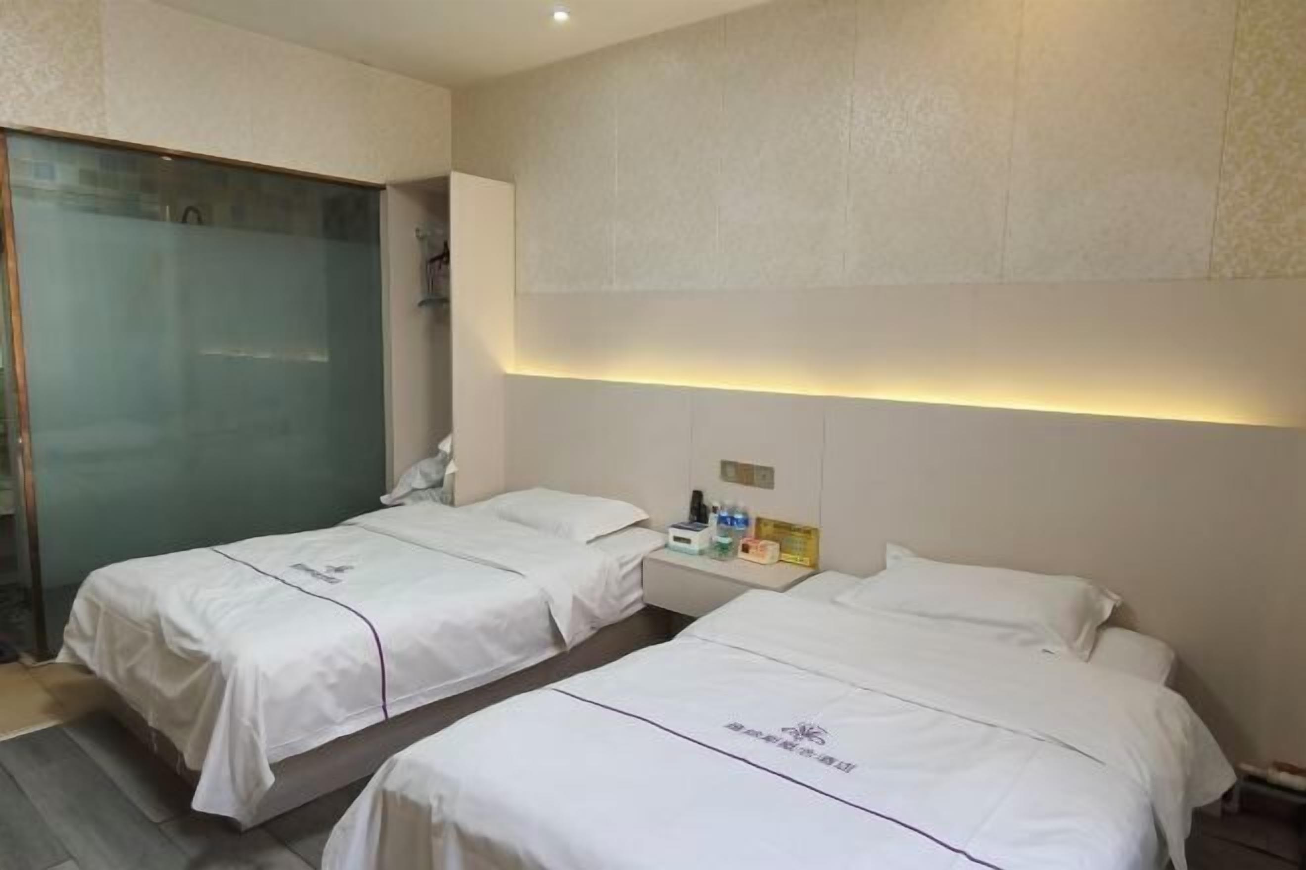 Une chambre d’hôtel avec deux lits, une douche en verre, une table de chevet avec des articles de toilette et une lampe fixée au mur.