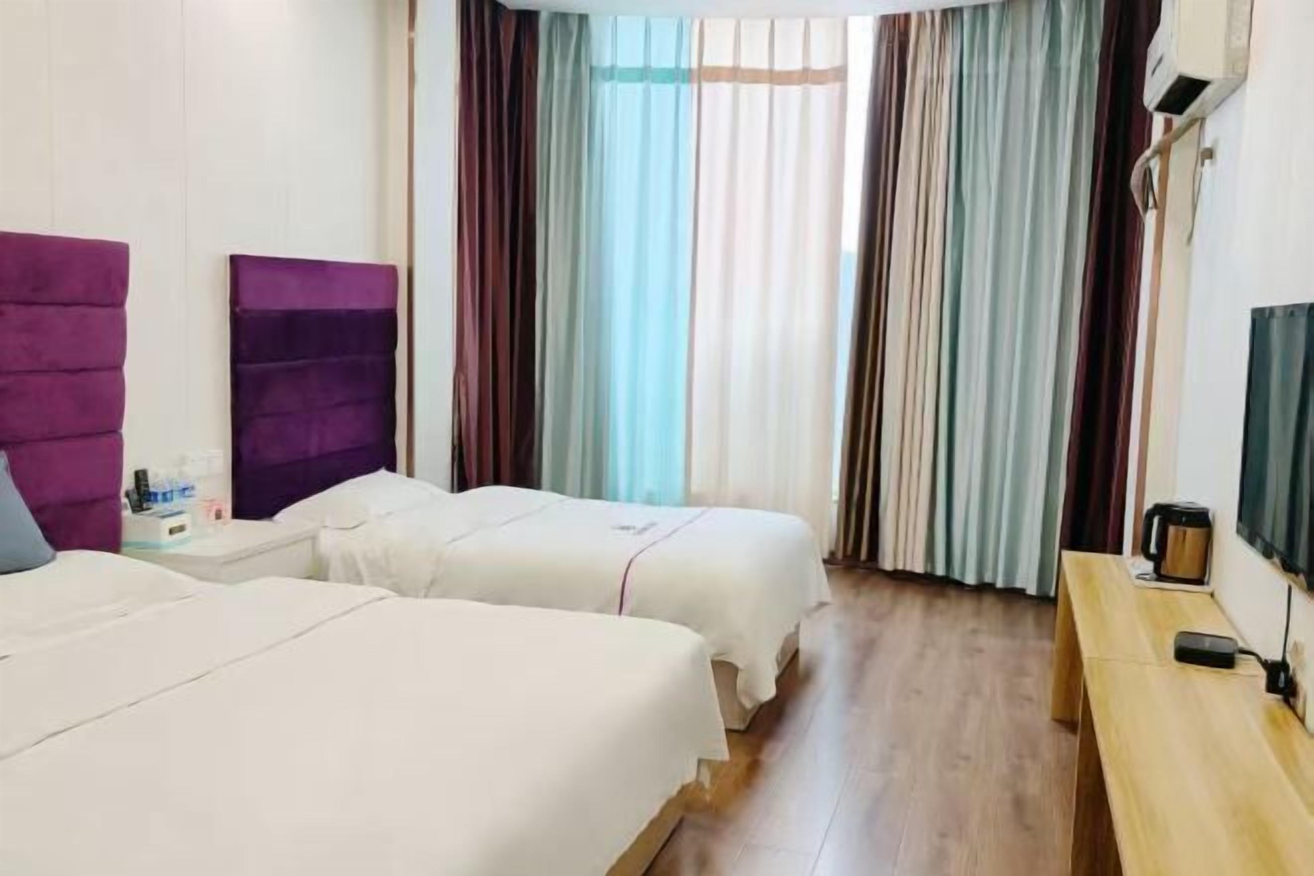 Ein Hotelzimmer mit zwei Betten, einer hölzernen Bank, einem Fernseher und einem Fenster mit Vorhängen.