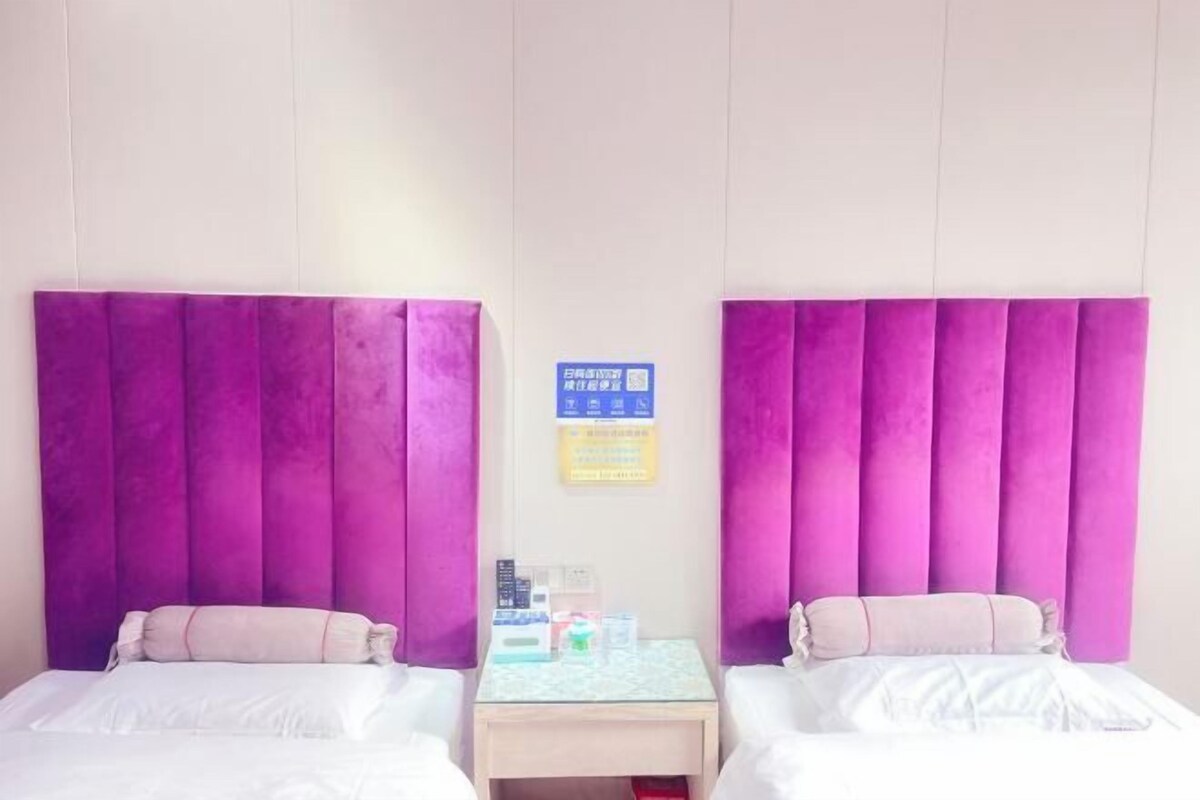 A hotel room with two beds, a small bedside table, and a sign on the wall.