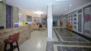 Un hall d’hôtel avec un sol en marbre, un comptoir d’accueil, des chaises et des éléments décoratifs, comme une statue de cheval et des œuvres d’art mural.