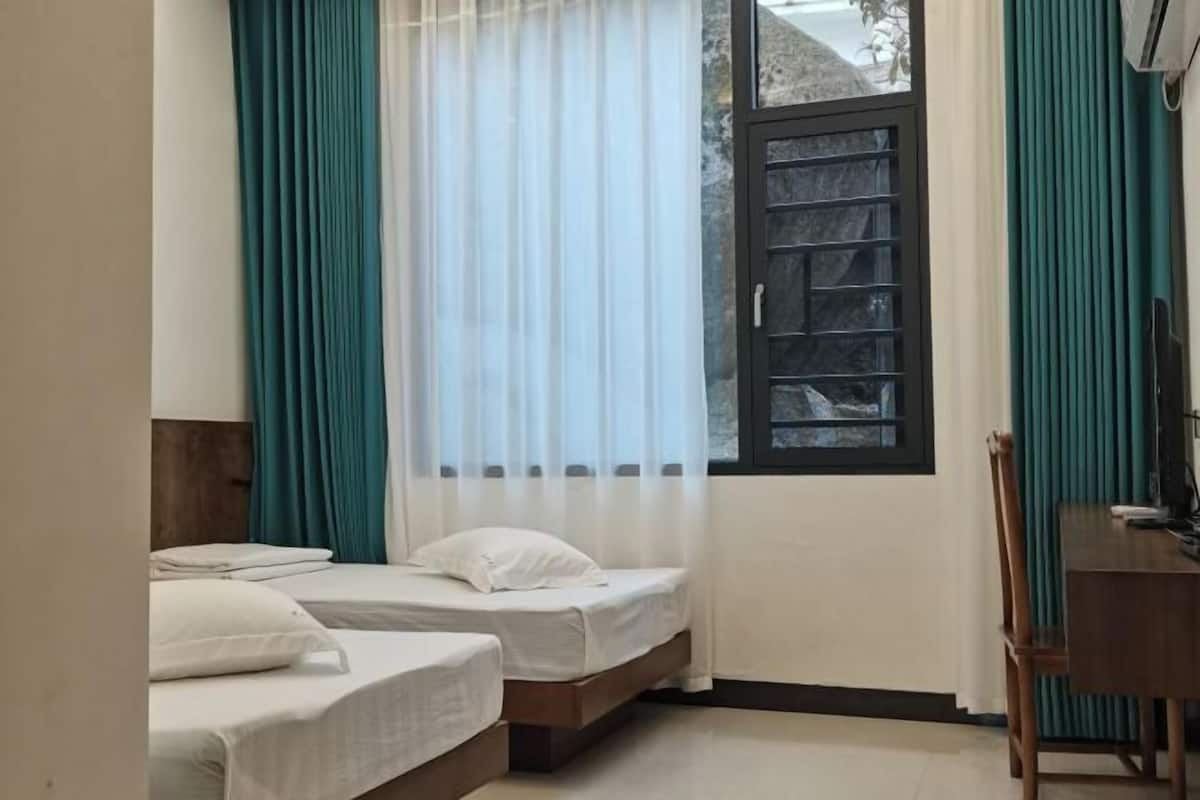 Quarto com duas camas, janela com vista e mesa de madeira.