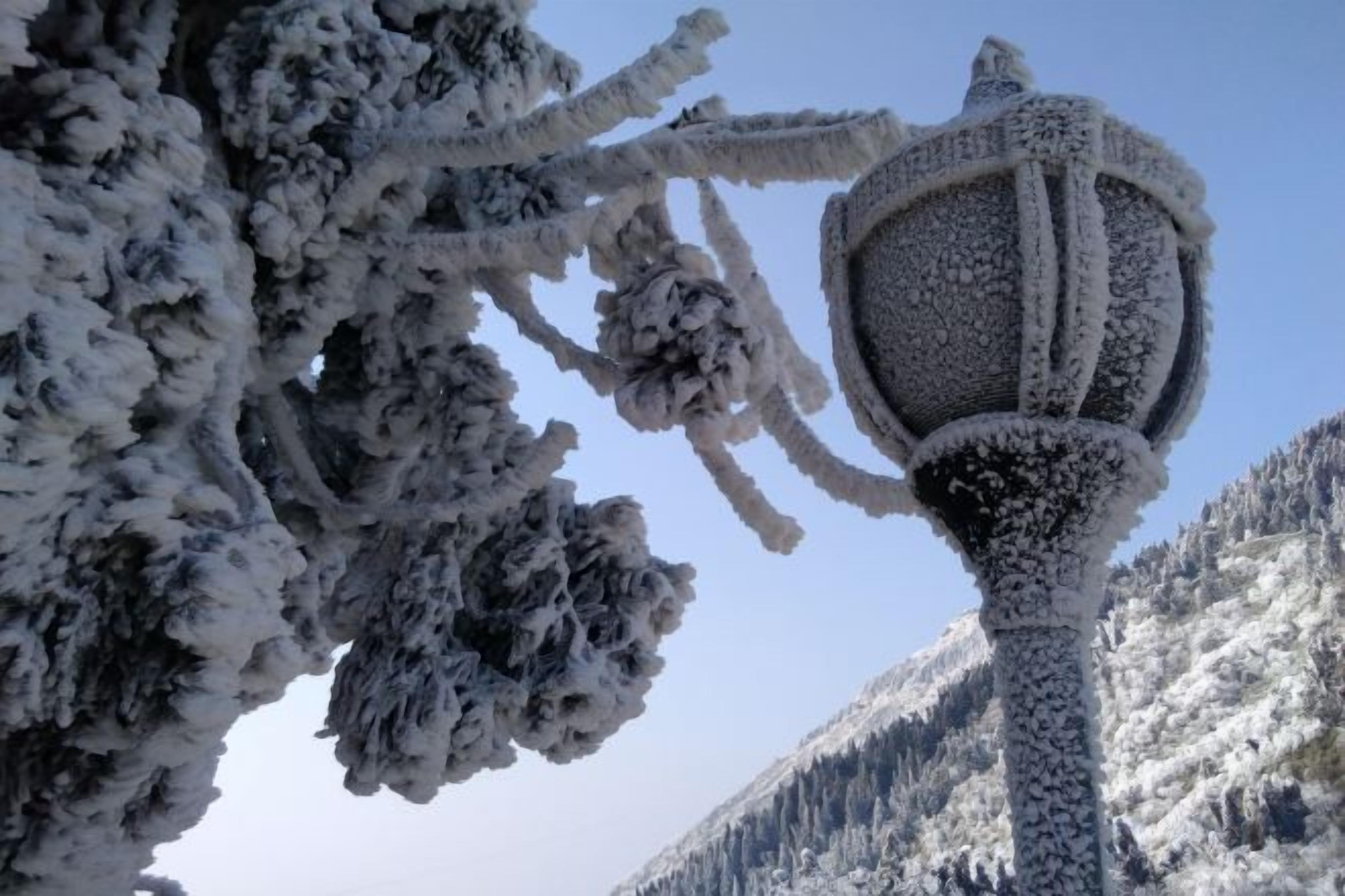 A snow-covered street lamp with a clear sky and mountains in the background.
