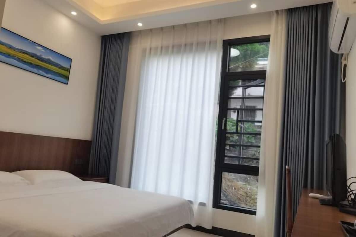 Quarto de hotel com cama, janela com cortinas, quadro na parede e televisão.