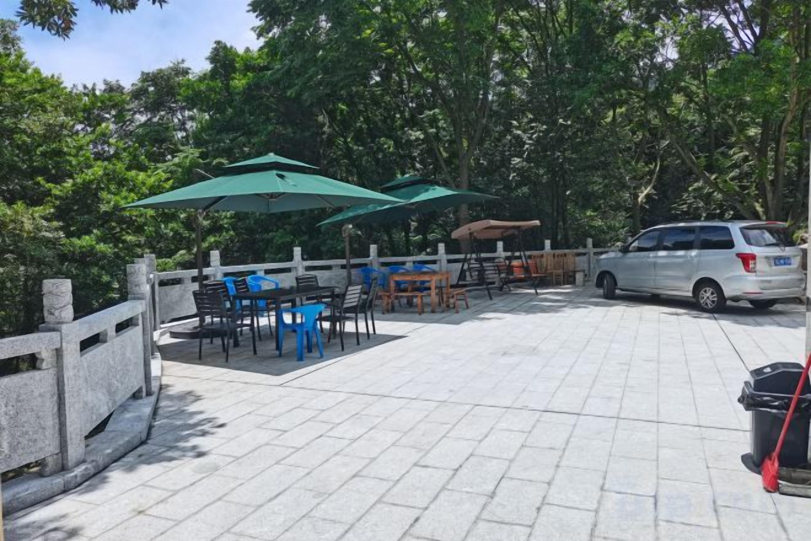 An outdoor patio area with tables and chairs, umbrellas, and a car parked nearby.