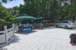 An outdoor patio area with tables and chairs, umbrellas, and a car parked nearby.