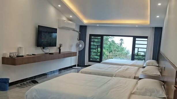 A hotel room with two beds, a TV, a fan, and a large window with a view of greenery. - Hengyang Nanyue Hengshan Qingshan Yunju (Hengyang)