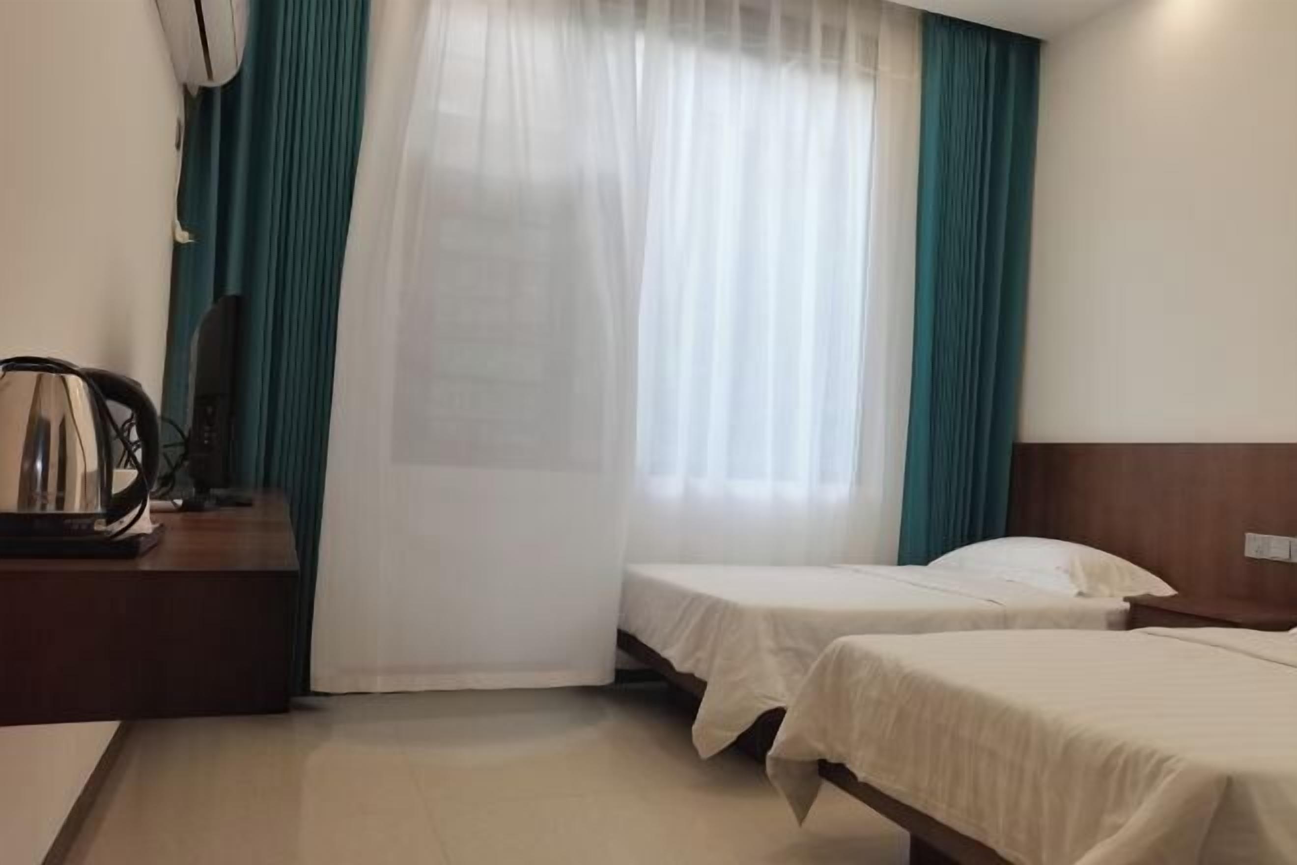 Habitación de hotel con dos camas, cabecera de madera, escritorio con lámpara y ventana con cortinas traslúcidas.
