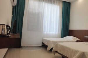Habitación de hotel con dos camas, cabecera de madera, escritorio con lámpara y ventana con cortinas traslúcidas.