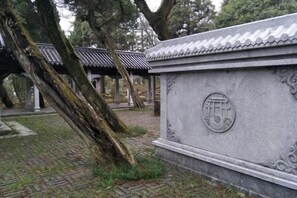 Un monumento in pietra con caratteri cinesi tradizionali, circondato da una struttura con tetto in tegole e alberi.