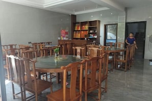 Un'area ristorazione di un hotel con tavoli rotondi e sedie in legno, una libreria e un'ampia finestra.