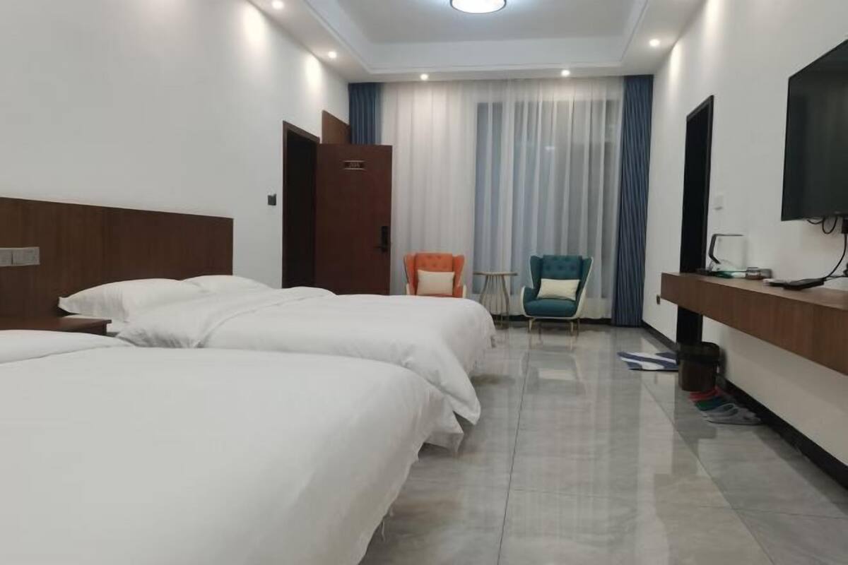 Quarto de hotel com duas camas, uma escrivaninha, uma cadeira, uma televisão e uma janela com cortinas.