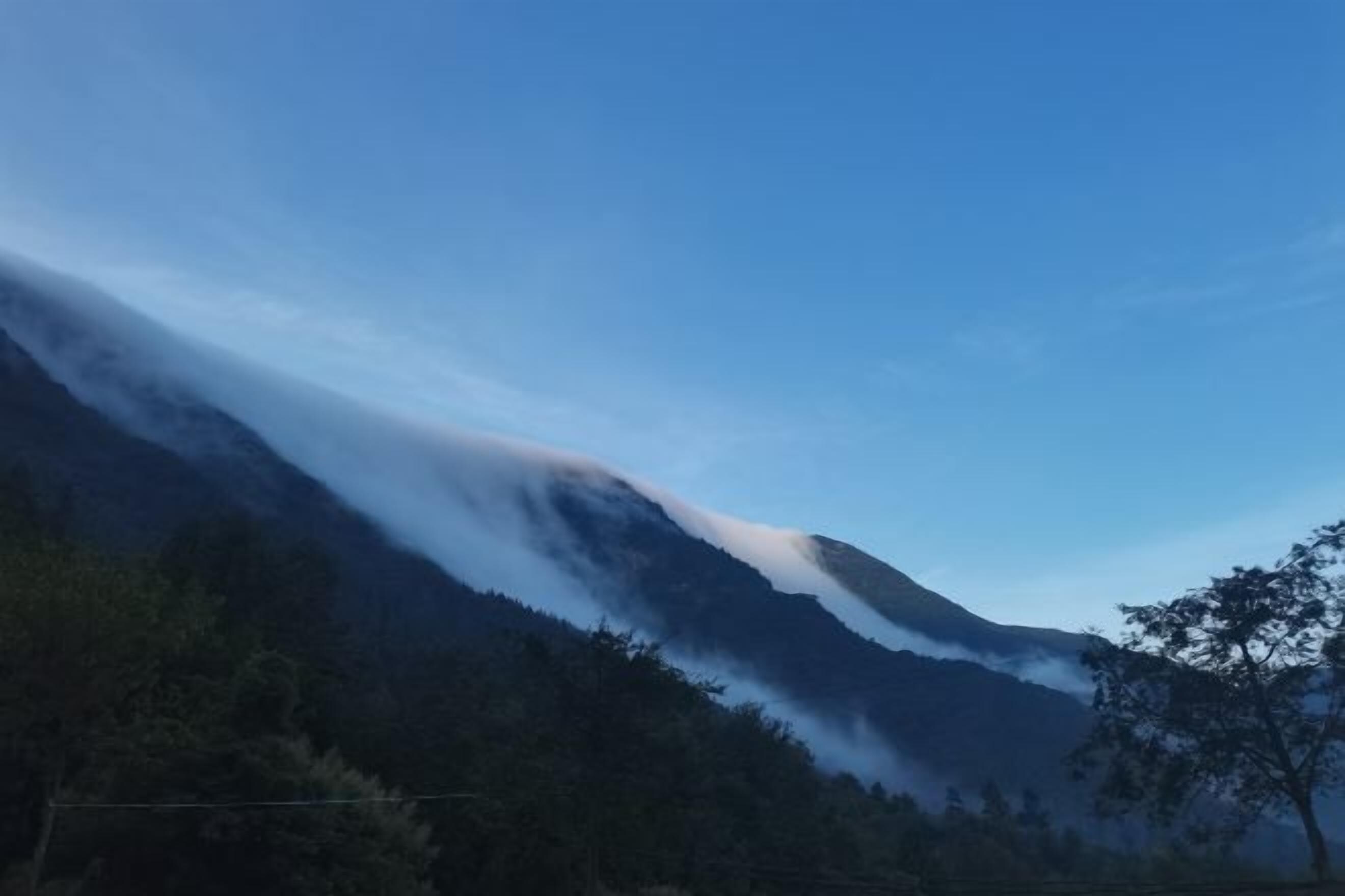 A mountain with a clear sky and a forested area at the base.