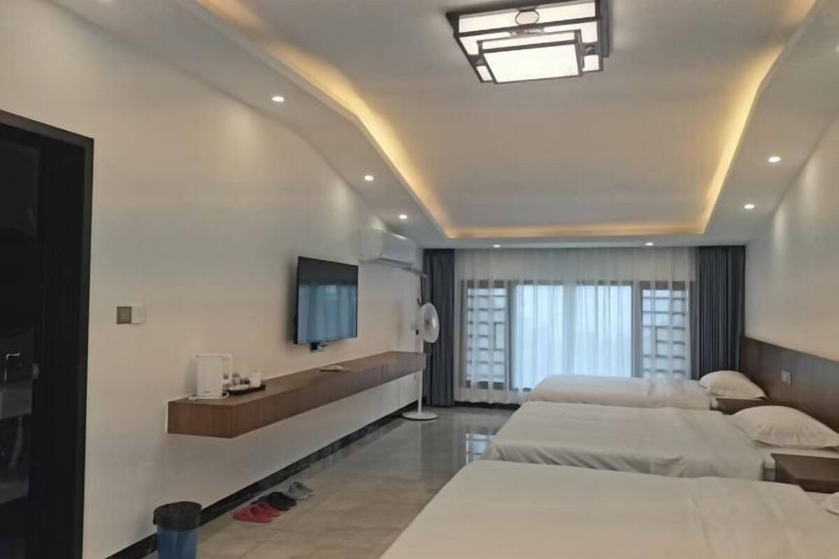Quarto de hotel moderno com uma cama grande, televisão, mesa de cabeceira e janela com cortinas.