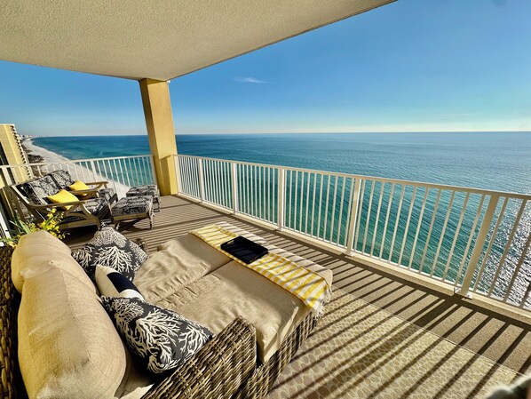 Un balcón con vista al océano, muebles de mimbre y un sofá con cojines.