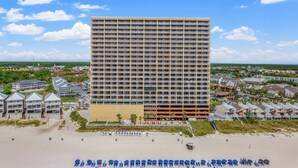 Un grand hôtel à étages, doté de nombreux balcons, situé près d’une plage où l’on trouve des rangées de chaises longues et de parasols.