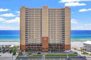 Un hotel de gran altura con varios balcones, un estacionamiento y vista a la playa.