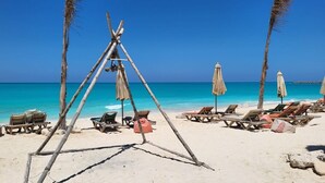 Une plage avec des chaises et des parasols en bois, une structure en bambou et des palmiers.