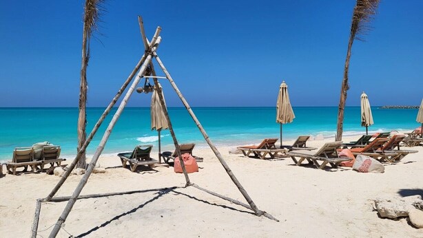 Ein Strand mit Holzstühlen und Sonnenschirmen, einer Bambuskonstruktion und Palmen.