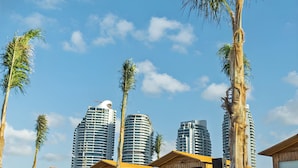 Ein Strandhotel mit Holzbungalows, Palmen und modernen Hochhäusern im Hintergrund.